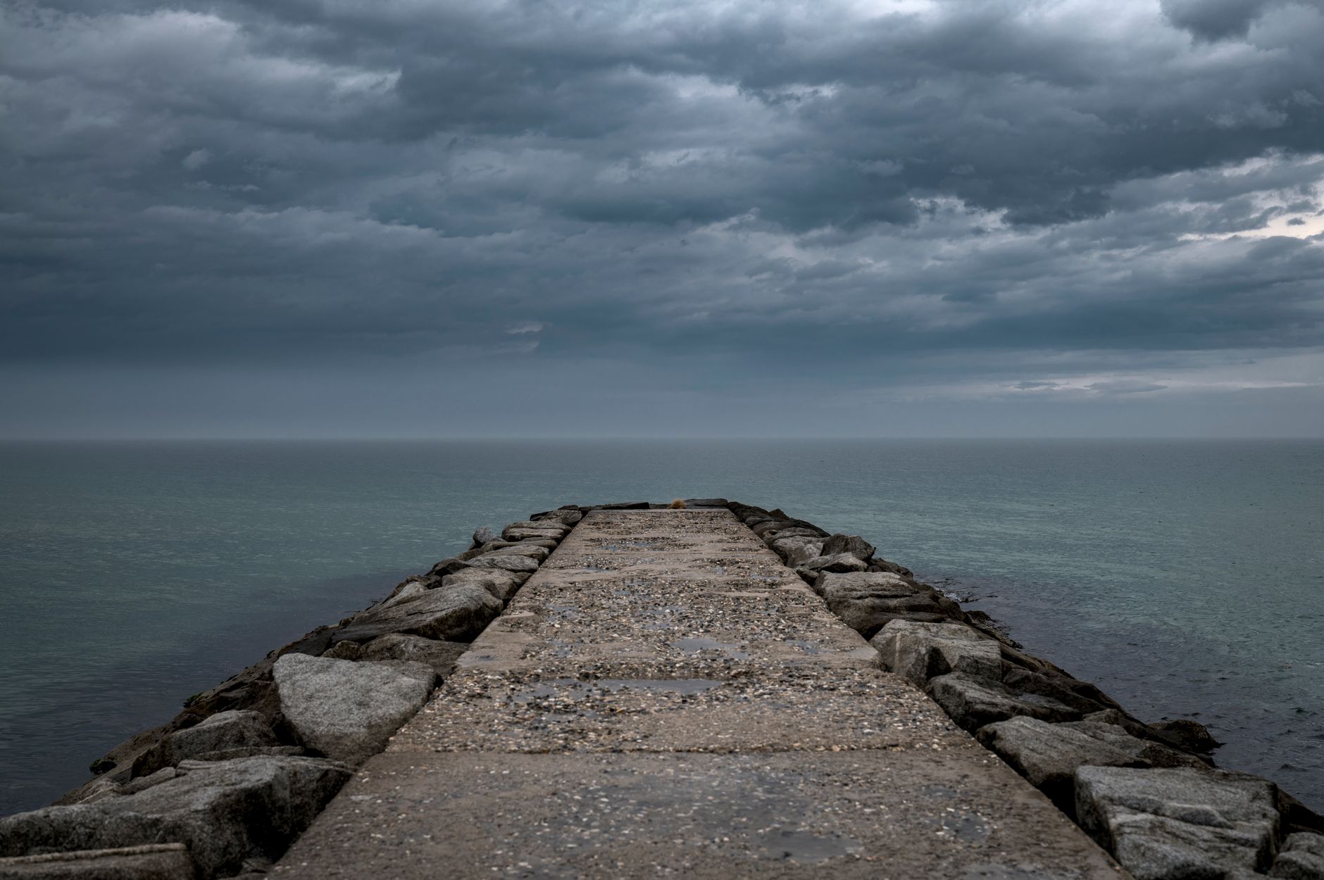 A captivating view of the stormy sea from a rock jetty under a cloudy sky in Gangneung, South Korea.